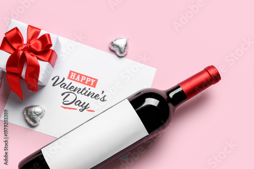 Card with text HAPPY VALENTINE'S DAY, bottle of wine, chocolate candies and gift box on pink background