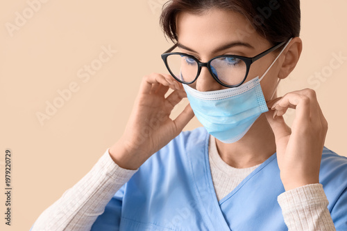 Female medical intern putting mask on beige background, closeup
