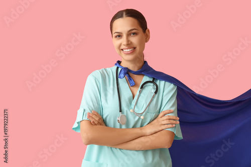 Beautiful female doctor in superhero costume on pink background