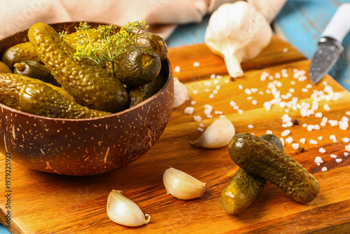 Bowl with tasty pickled cucumbers and different spices on blue wooden background