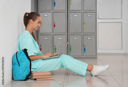 Female medical student studying with laptop near locker at university