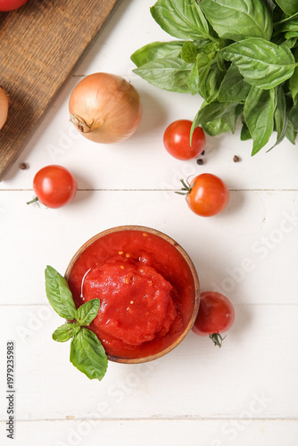 Bowl of canned tomatoes and spices on light wooden background