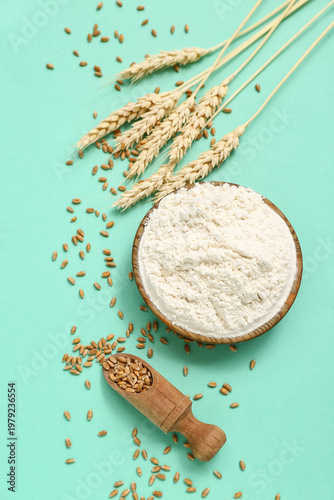 Bowl with wheat flour, scoop and spikelets on turquoise background