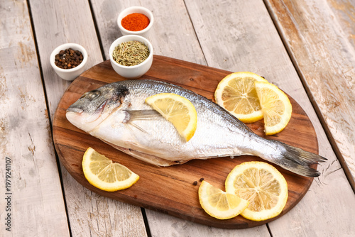 Board of raw dorado fish with lemon on grey wooden background