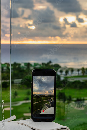 A smartphone captures a stunning coastal sunset over waves, showcasing the beauty of nature, reflections, and vibrant colors against a serene landscape in the background.