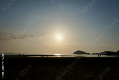 Canvastavla Silhouetted People Walking on Beach at Sunset With Distant Island and Calm Sea