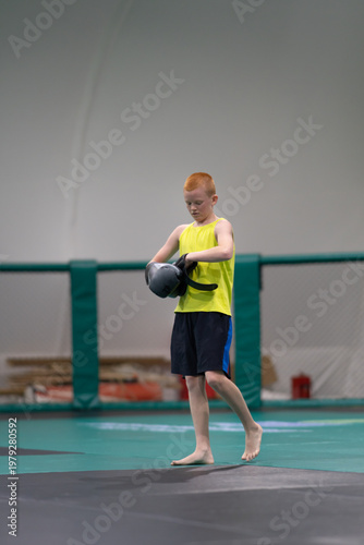 A teenager warms up during a martial arts training session on the tatami mat in a gym and puts on boxing gloves. High quality photo