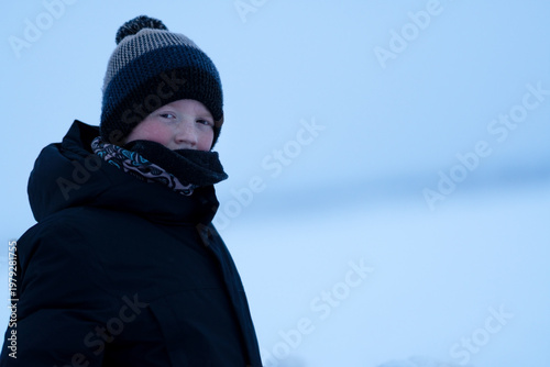 A teenager in winter clothes against a snowy winter backdrop of the sea. A boy with rosy cheeks on a nature walk. Concept of recreation, sports, and people. High quality photo