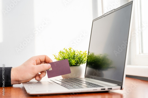 Person holding a credit card while using a laptop for online shopping and financial transactions, close-up 
