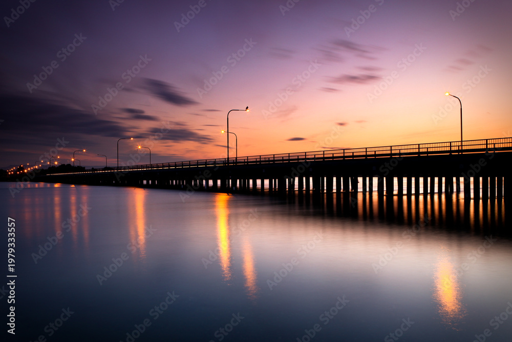 Fototapeta premium Silhouette of the iconic Windang Bridge, connecting the suburbs of Lake Illawarra south and Windang, captured with a long exposure as the sun retreats leaving a golden glow in the west. 