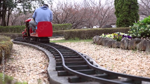 Child enjoying a ride on a small steam locomotive at a public park, focus on the moving train and wheels.