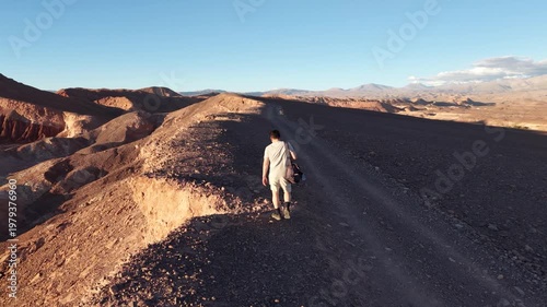Cinematic drone shot follows TV Host of DIY Destinations Charles Huang as he walks along a narrow desert ridge in the Mars Valley (Valle de Marte) near San Pedro de Atacama, Chile, during golden hour