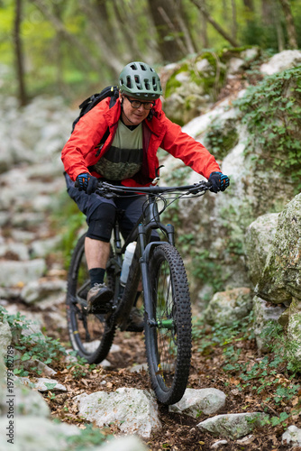Man mountain biking on rocky forest trail wearing helmet and red jacket for outdoor adventure