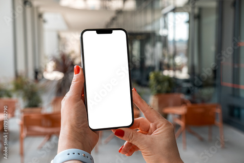 Mockup woman's hand holding using smart phone with white blank screen POV at coffee shop, mobile app design and advertising, online marketing