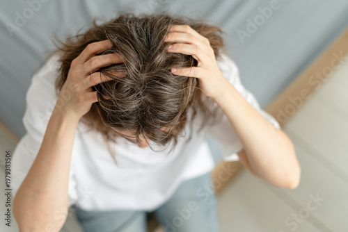 A woman reacts with surprise to suddenly discovering new gray hairs on her head. The mature adult was not expecting silver strands to appear so quickly. Mother faces unexpected sign of aging.