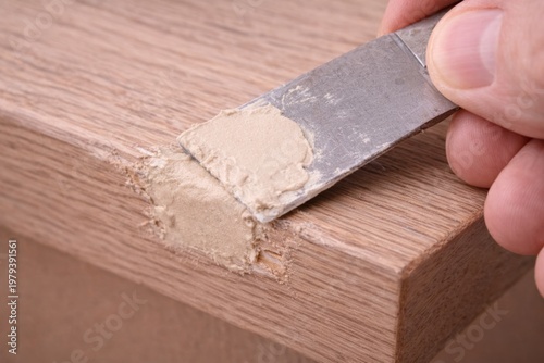 Repairing Wooden Furniture Corner with Wood Putty. Applying beige wood filler to chipped furniture corner using metal spatula tool.