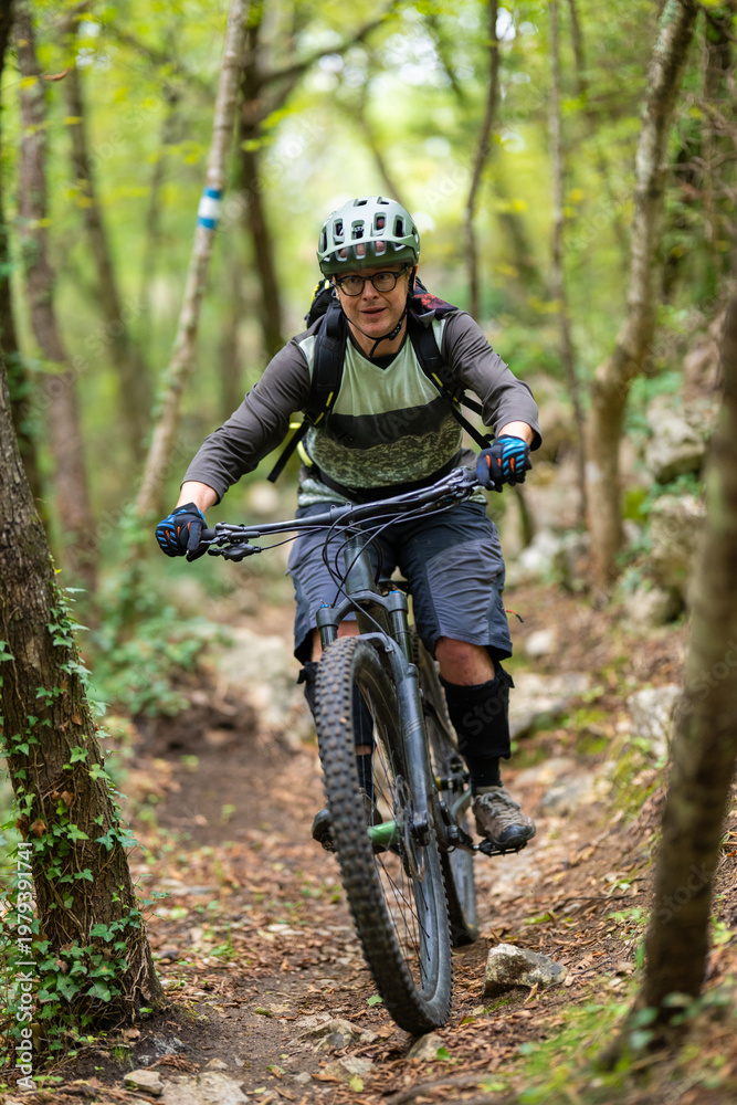 Fototapeta premium Experienced cyclist mountain biking on a rocky forest trail wearing helmet and protective gear