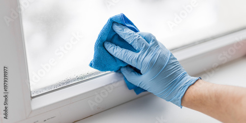 Obraz na plátně Gloved hand wiping wet window sill near closed pane