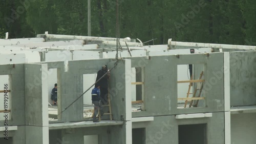 Detailed view of construction workers building multistory apartment complex. One worker performs welding on metal joint of concrete panels, sparks visible. Other workers assemble structure. Active con