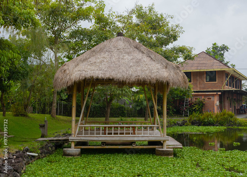 Traditional bamboo gazebo with thatched roof standing over a green aquatic pond
