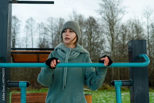 Close-up shot of a sporty womans face and hands as she tightly grips the handlebar of an outdoor leg trainer. moment of maximum effort, showcasing dedication to winter fitness and strength.