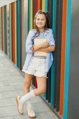 Smiling child with book leaning on colorful outdoor school wall