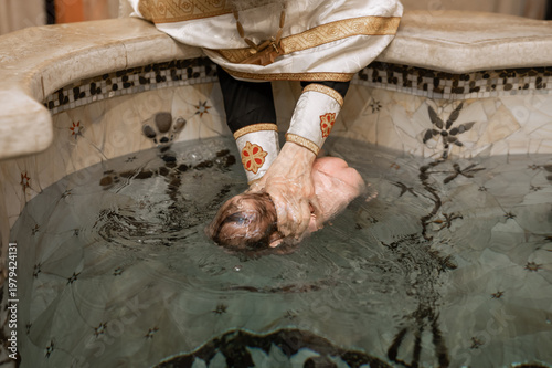 Orthodox Priest Dipping Newborn Baby into Holy Water Font During Baptism Ceremony in Church Interior