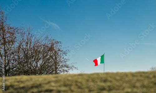 Italian national flag waving above rural landscape under clear sky symbol of identity.
