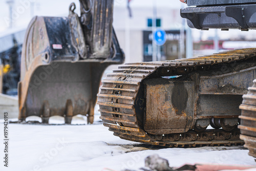 Close up of excavator steel tracks on snowy construction site in winter.