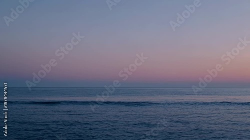 Serene ocean waves gently rolling towards the shore at dusk, with a gradient sky transitioning from soft pink to deep blue over the calm water surface