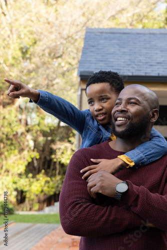African American father and son standing on deck in yard, father wearing watch, child pointing left