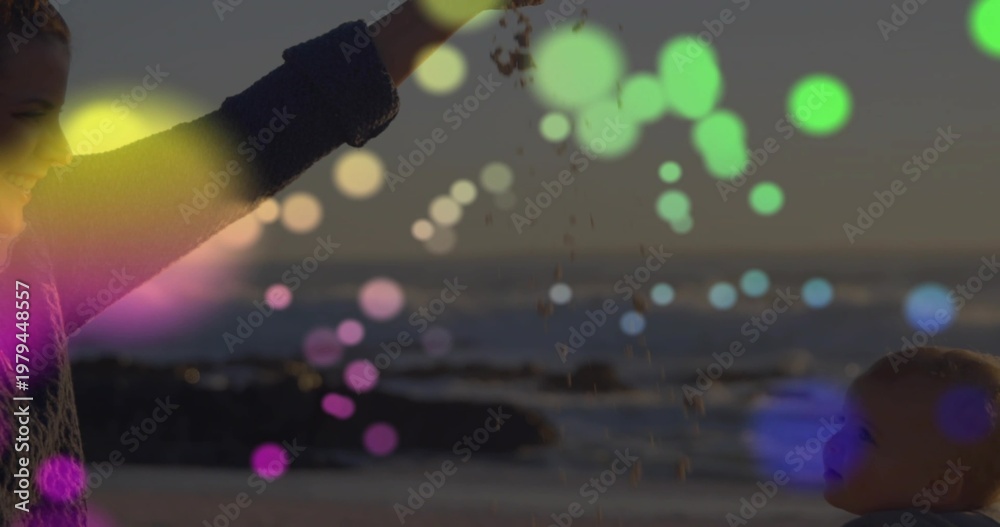 Obraz premium Caregiver and infant interacting as caregiver lifting arm, releasing sand with bokeh at dusk beach
