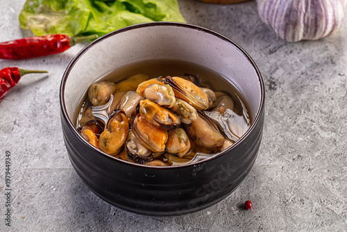 Cuadro en lienzo Marinated mussels in a bowl with fresh garlic, chili, and lettuce on a rustic st