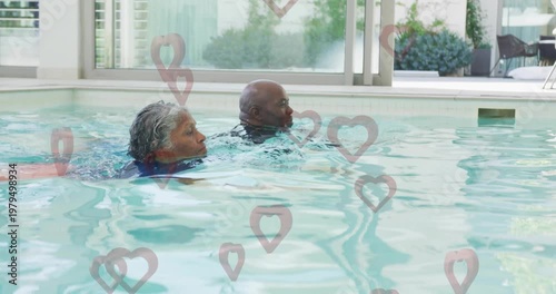 Elderly couple swimming in indoor pool with heart shapes overlay animation