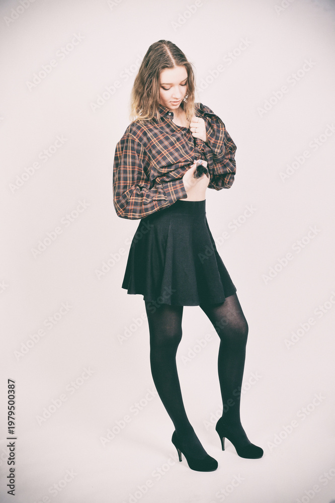 Fototapeta premium Blondes Model im Outfit mit Rock und Strumpfhose, nachdenkliche Pose, modernes Fashion- und Lifestyle-Porträt im Studio isoliert