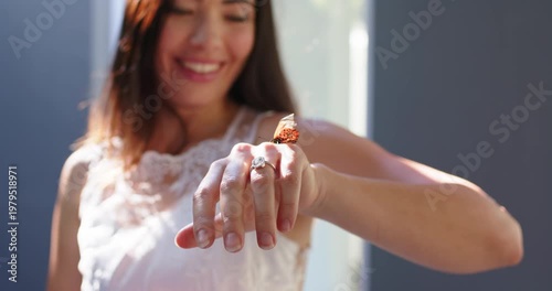 Woman in white-lace top holding hand, monarch butterfly coming, landing on ring, watching by window