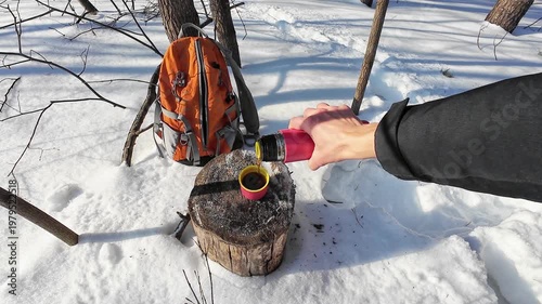 Outdoor Coffee Break Scene. Person Enjoys Hot Drink On Snowy Trail. Hiker At Rest Pours Warm Beverage Into Cup Amidst Snow. Individual In Woods Takes Moment To Sip Steaming Coffee On Snowy Day