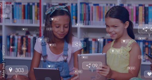 Reading 2 girls wearing denim overalls and yellow dress holding tablets in library showing UI icons