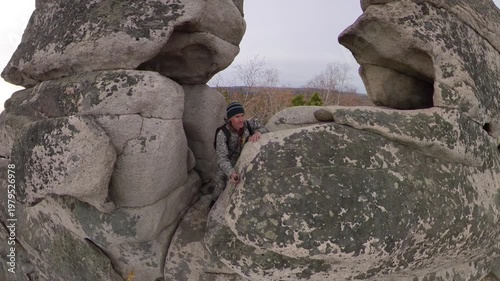 A man on a cliff. 2 Shots. A tourist admires the picturesque autumn view of the forest and lake from the top of a mountain, standing among granite boulders.