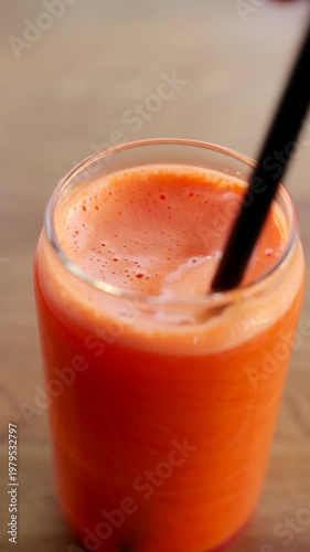 Fresh orange juice being stirred into a glass with a straw creating foam and bubbles