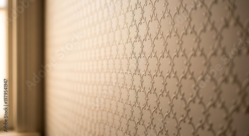 A close-up view of a beige wall with a patterned wallpaper and a window frame in the background