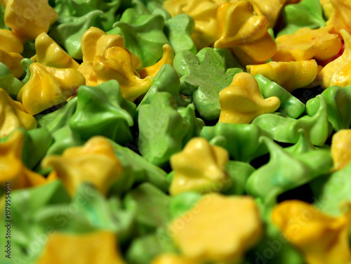 Meringue cookies in green and yellow shapes on a baking tray during a dessert preparation