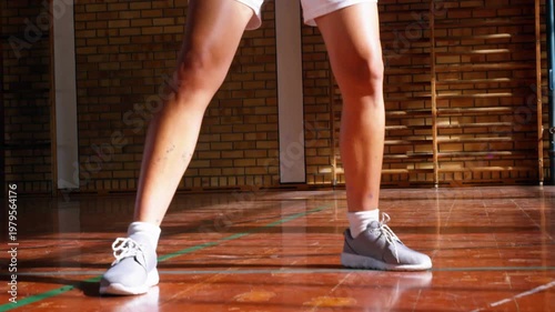 Teen practicing dribbling in sports court, orange ball bouncing into frame between legs training