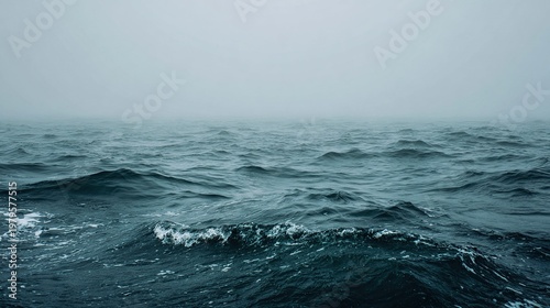 Misty seascape featuring gentle waves disappearing into a hazy horizon under a gray sky