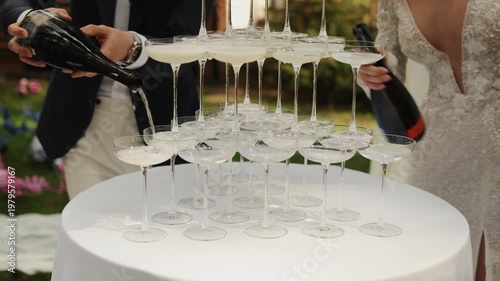The bride and groom pour champagne into a pyramid of glasses, the couple pours champagne at their wedding