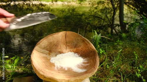 Male hand pouring flour from knife on wooden bowl. Close-up of baker preparing ingredients for recipe at outdoors. Artisanal cooking concept