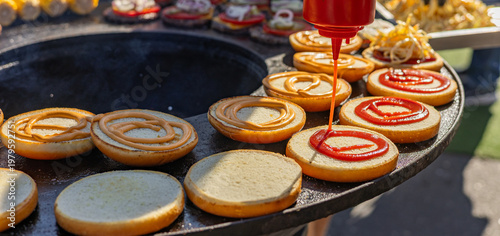 Принти на полотні A food vendor generously squirting ketchup onto a toasted burger bun