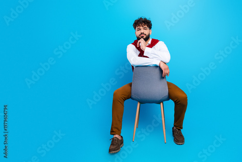 Photos Casual young man sitting backwards on a chair against a bright blue background,