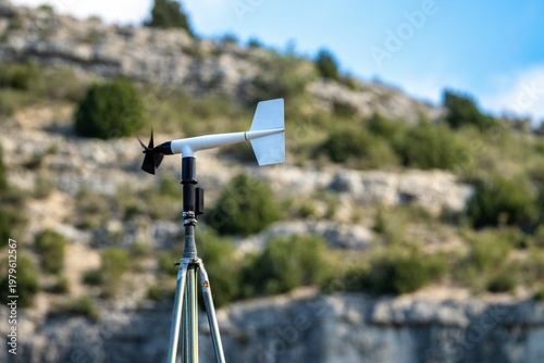 White Anemometer and Wind Vane with Black Propeller Against Blurry Rock Background