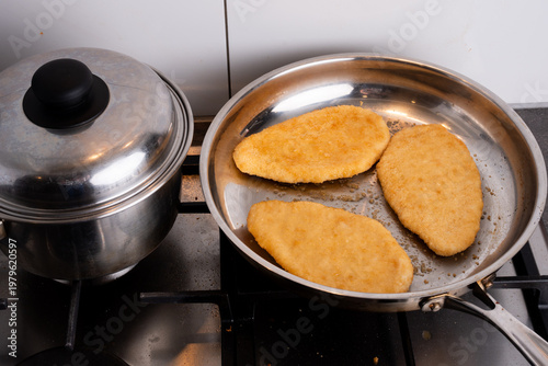 three chicken schnitzel being fried on the stove